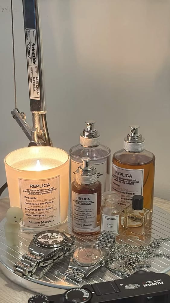 A lit candle and perfume bottles above silver watches, jewelry, and a Fujifilm camera on a tray