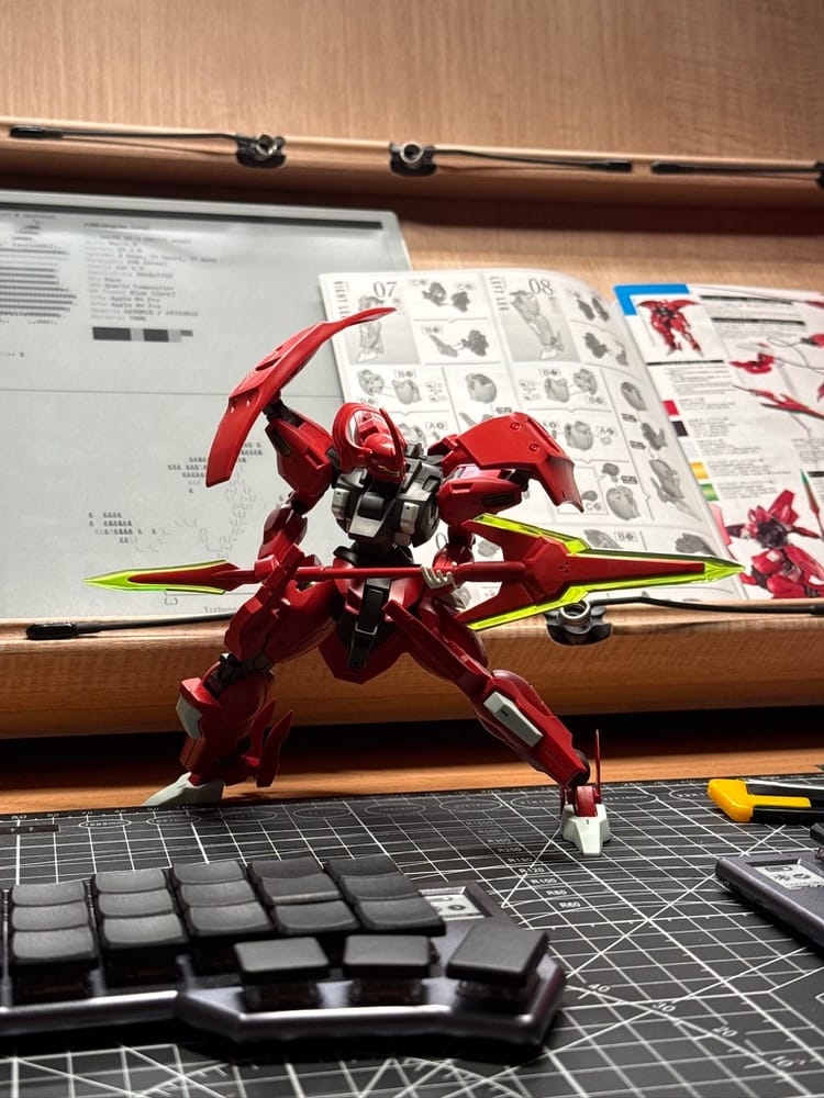A red Darilbalde model posed with green blades on a cutting mat in front of its assembly instructions